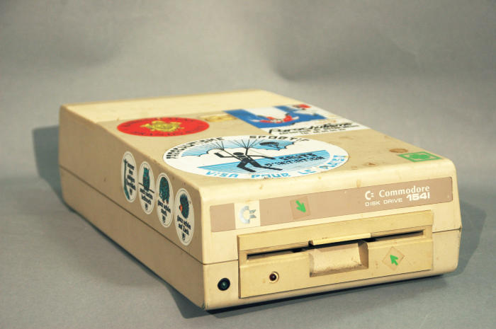 The Commodore 1541 (also known as the CBM 1541 and VIC-1541) is a floppy disk drive (FDD) which was made by Commodore International for the Commodore 64 (C64), Commodores most popular home computer. The best-known FDD for the C64, the 1541 was a single-sided 170 kilobyte drive for 5¼- disks. The 1541 followed the previous Commodore 1540 (meant for the VIC-20).The 1541 was priced at under US$400 at its introduction. A C64 plus a 1541 cost about $900, while an Apple II with no disk drive cost $1395: the 1541 became widely popular; The demand caught Commodore by surprise, and the company struggled to produce the drive in adequate quantities.[citation needed]

The first 1541 drives produced in 1982 had a label on the front reading VIC-1541 and had a white case to match the VIC-20. Failure rates on the 1541 initially were very high,[quantify] and the drives were virtually impossible to find. The lead editorial in the December 1983 issue of Computes Gazette lamented that four of the seven drives the magazine had in its editorial offices had failed. Eventually the problems subsided and the drive became nearly as widely available as the C64 itself. In 1983, the 1541 switched to the familiar gray case and a front label reading simply  1541 along with rainbow stripes to match the Commodore 64.

The early (1982–83) 1541s had a spring eject mechanism (Alps Drive), and the discs often failed to release. This style of drive had the popular nickname Toaster Drive, because it required the use of a knife or other thin object to pry out the stuck media just like a piece of toast stuck in a real toaster (though this is inadvisable with real toasters). This was fixed later, when Commodore changed the vendor of the drive mechanism (Mitsumi) and adopted the flip-level Newtronics mechanism, greatly improving reliability. In addition, Commodore made the drives controller board smaller and reduced its chip count compared to the early 1541s (which had a large PCB running the length of the case, with dozens of TTL chips). The gray-case Newtronics 1541 was produced from 1984-86.

The disk drive used Group Code Recording (GCR) and contained a MOS Technology 6502 microprocessor, doubling as a disk controller and on-board disk operating system processor. The number of sectors per track varied from 17 to 21 (an early implementation of Zone Bit Recording). The drives built-in disk operating system was CBM DOS 2.6.
Quelle: http://en.wikipedia.org/wiki/Commodore_1541

Commodore 1541-II Floppy Disk Drive. Die VC 1541 ist ein 5,25-Zoll-Diskettenlaufwerk für den Heimcomputer C64 von Commodore. Sie kam 1982 auf den Markt und wurde das erfolgreichste Modell der VC15xx-Serie. Die 1541 besitzt nur einen Schreib/Lese-Kopf und kann daher Disketten nur einseitig beschreiben. Um die volle Kapazität einer Diskette zu nutzen, kann man diese zum Beispiel mittels eines Diskettenlochers mit einer zusätzlichen Schreib/Lese-Kerbe an der linken Seite versehen. Auf einer solcherart modifizierten Diskette können dann durch Umdrehen weitere 165 KB gespeichert werden.
Quelle: wikimedia.org/wikipedia/commons/b/bb/Commodore_1541_white.jpg&imgrefurl=http://de.wikipedia.org/wiki/VC1541&h=1333&w=2000&sz=375&tbnid=_WhFpDoKYcHiBM:&tbnh=94&tbnw=141&zoom=1&usg=__P87sxREguwLb8Nt84cAltS2z8gU=&docid=dW1wFbf00x5gkM&sa=X&ei=pRn2Upa5I4bVt

