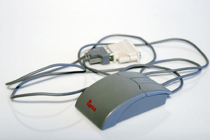 Eine mechanisch-elektrische, kabelgebundene Maus mit einer Gummikugel. Angeschlossen ein Adapter zum Anschluß an wahrscheinlich schon aktueller PC-Peripherieslots
